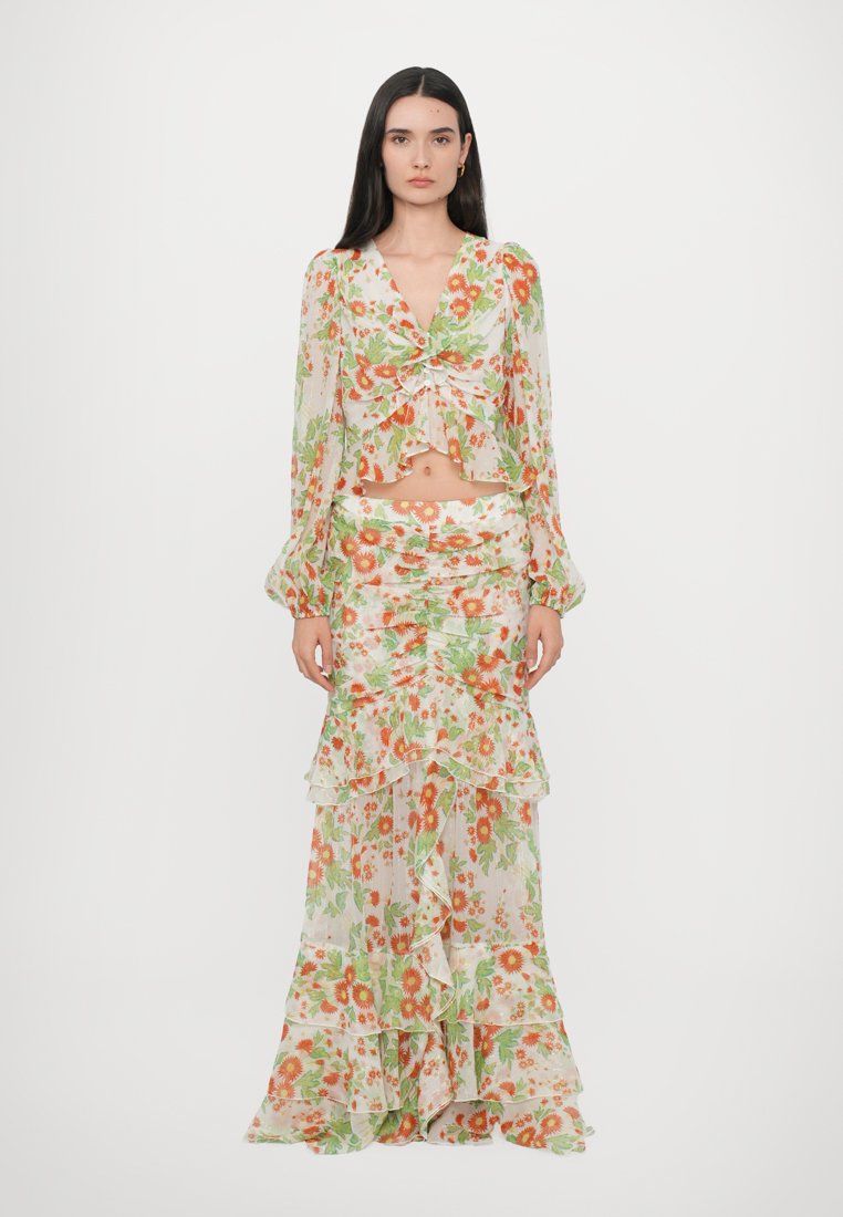 Ensemble floral composé d'un top transparent à manches longues à volants avec un nœud devant et d'une jupe assortie longue au sol avec des couches superposées.