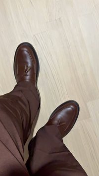 Asmuo dėvi rudus kutas batus ir derančias rudus kelnes, stovinčias ant šviesios medinės grindų dangos.