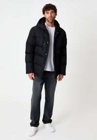 Doudoune noire avec capuche, poches zippées et fermeture à pression. Associée à un jean gris et des baskets blanches. Design simple et pratique.