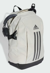 Sac à dos gris clair avec une base noire, comportant trois rayures verticales noires, des bretelles ajustables et un porte-bouteille latéral.