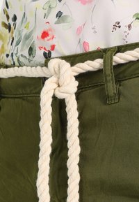 Olivgröna byxor med en jämn textur, med ett elfenbensfärgat repbälte knutet i midjan. Blommig topp delvis synlig ovanför.