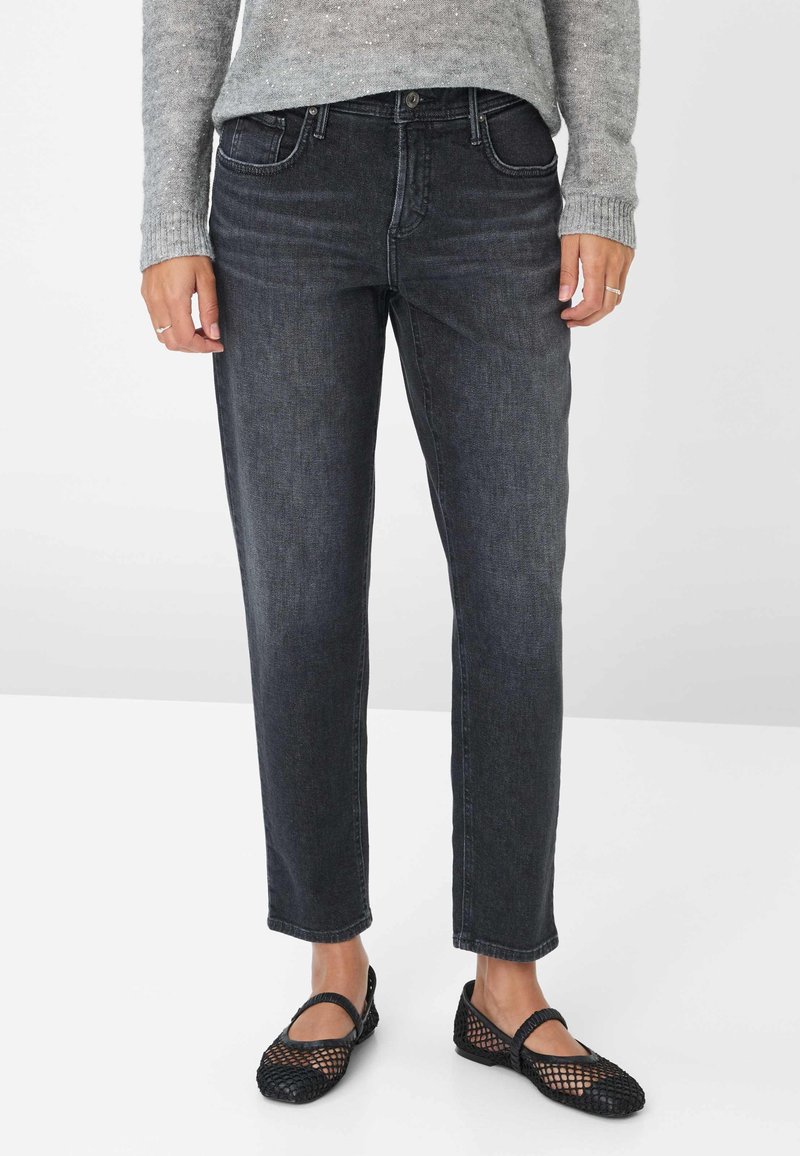 Jean en denim noir à coupe droite, avec cinq poches et détails de couture. Associés à des chaussures plates en maille noires. Le pull est de couleur gris clair.