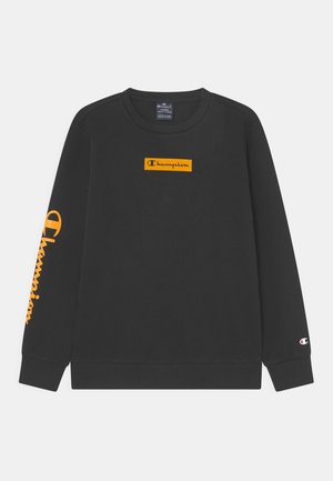 Czarna bluza Champion z długim rękawem, z pomarańczowym prostokątnym logo na piersi oraz dużym pomarańczowym napisem Champion na lewym rękawie.