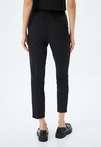 Zwarte, slim-fit broek met een soepele textuur, enkelhoogte en twee achterzakken. Gemaakt in combinatie met chunky zwarte schoenen.