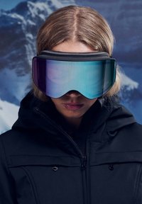 Skibrille mit einer breiten, gebogenen Linse, die einen Farbverlauf von Lila zu Türkis aufweist. Weicher schwarzer Rahmen und eine dunkle, strukturierte Jacke sind sichtbar.