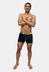 Svarta boxershorts med en gul "MR UKKO" midjeband, tillverkade av ett slätt material, med en figurnära design och minimalistisk stil.