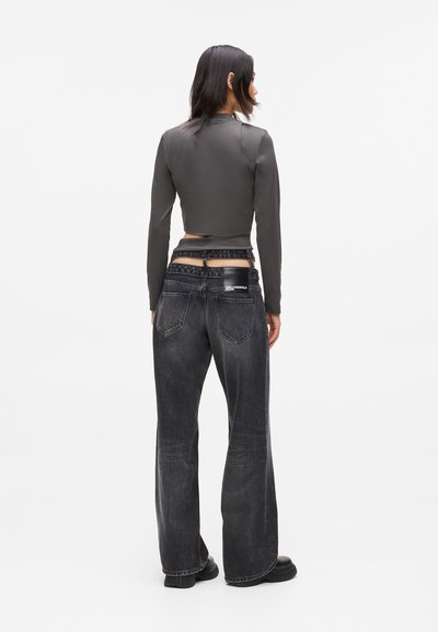 Jean flare noir taille haute avec un délavage léger ; associé à un haut ajusté à manches longues gris foncé et cropped. Détails de tissu texturé visibles.