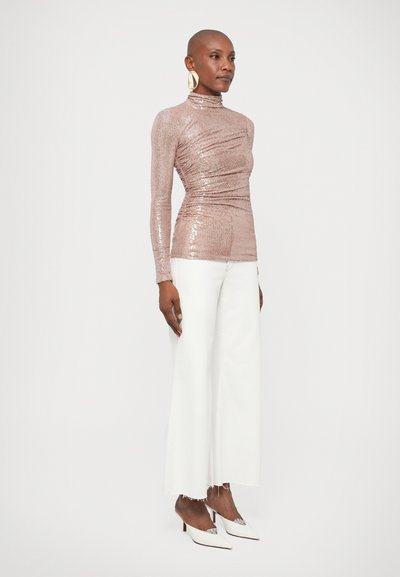 Λαμπερή, εφαρμοστή μπλούζα μακρύ μανίκι με ροζ χρυσές παγιέτες, συνδυασμένη με λευκά παντελόνια καμπάνα σε cropped γραμμή και λευκές ψηλοτάκουνες γόβες. Χρυσά σκουλαρίκια κρίκοι ολοκληρώνουν την εμφάνιση.