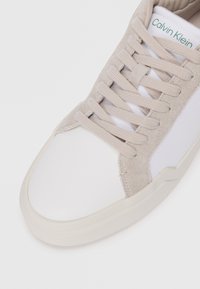 Witte sneaker met grijze suède accenten, platte veters en een rubberen zool. Beschikt over een logolabel op de tong. Glad oppervlak met subtiel kleurcontrast.