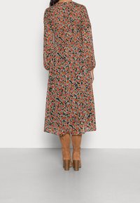 Vestido largo de flores con base negra y flores rojas y blancas, mangas largas y una silueta fluida, combinado con botas de caña alta color marrón claro.