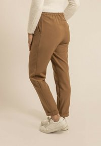 Pantalons marron �à taille élastique avec poches latérales et jambes fuselées, en tissu lisse, associés à des baskets blanches.