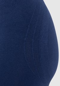 Tmavě modrá podprsenka s hladkým materiálem, konturovaným střihem a texturovanými bočními panely. Vyznačuje se čistými liniemi a minimalistickým designem.