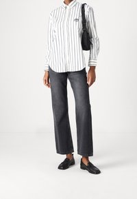 Vit skjorta med svarta vertikala ränder, som kombineras med mörka raka jeans och svarta loafers. Inkluderar en svart axelremsväska.