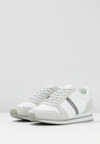 Baskets blanches et grises avec une finition en cuir lisse et en suède, dotées de lacets gris, d'une marque sur le côté et d'une semelle texturée.