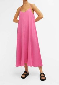 Robe rose sans manches à coupe ample et tissu texturé, avec un décolleté en V et une longueur au genou. Associée à des sandales noires.