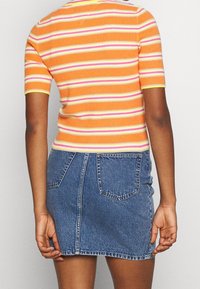 Top naranja de manga corta con textura acanalada y rayas rosas y amarillas, combinado con una mini falda de mezclilla azul que cuenta con dos bolsillos traseros y un cierre.