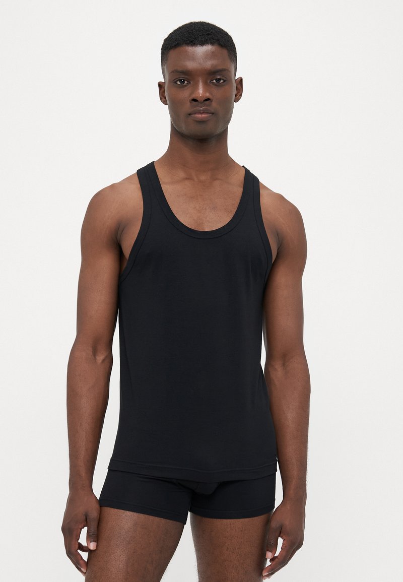 Schwarzes Tank-Top aus einem glatten, dehnbaren Stoff. Mit breiten Trägern, Rundhalsausschnitt und einer taillierten Passform. Kombiniert mit schwarzen Boxershorts.
