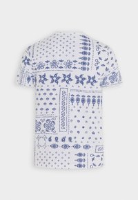 Lyhythihainen valkoinen T-paita, jossa on monimutkaisia sinisiä kukka- ja geometrisia kuvioita. Pehmeä, kevyt kangas ja rento istuvuus.