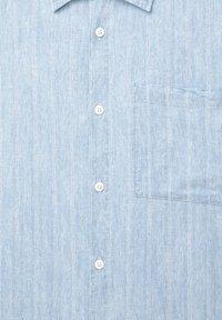 Camicia azzurra chiaro con botonatura in tessuto testurizzato, caratterizzata da strisce verticali, una tasca sul petto e bottoni bianchi.