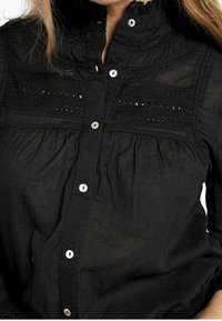 Chemise noire boutonnée en tissu léger, avec un col montant, des détails en dentelle élaborée et des boutons en nacre.