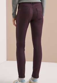 Bordeaux skinny jeans met twee achterzakken, een gladde stofstructuur, een middelhoge taille en een slanke pasvorm. Gestyled met lichtgekleurde sneakers.