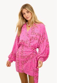 Robe portefeuille imprimée paisley rose avec manches longues, col en V et ceinture nouée. Présente des motifs complexes dans différentes nuances de rose et de rouge.