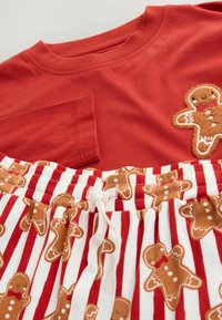 Rød bomulds t-shirt med en peberkagemand broderet på brystet, parret med hvide og røde stribede shorts med peberkageprint.