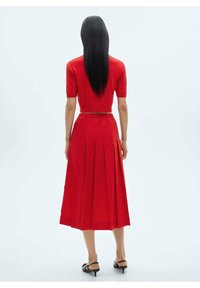 Conjunto de dos piezas rojo que incluye un crop top ajustado con mangas cortas y una falda midi plisada de cintura alta. Textura suave, diseño minimalista.