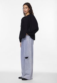 Svart blus med långa ärmar och samlad midja, strukturerad tyg; parat med ljusblå högmidjade jeans med ett hål vid knäet.