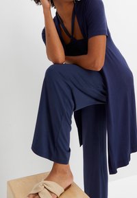 Conjunto de loungewear en azul marino compuesto por una camiseta de manga corta, pantalones de pierna ancha y un cárdigan largo, combinado con sandalias tipo slide texturizadas en color beige.