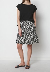 Haut noir à manches courtes associé à une jupe à motifs blancs et noirs, avec une coupe décontractée, une taille élastique et des poches latérales. Sandales à glisser noires.