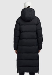 Must musternööpidega must sulejope, millel on pikk soe disain, suur kapuuts ja horisontaalne tikanditöö. Tõmblukkude detailid hemil.