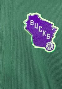 Groene stof met een paars silhouet van de staat Wisconsin logo met de tekst "BUCKS" en een basketbalicoon, omlijst door een lichtgroene rand.