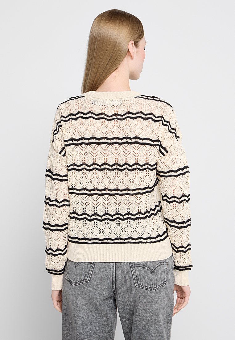 Gebreide trui in roomkleur met zwarte strepen. Voorzien van een opengewerkte patroon en geribbelde boorden. Relaxte pasvorm met een ronde halslijn en textuurdetail.