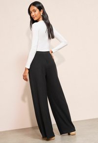 Melni riboti platajiem svārkiem ar augstu vidukli, kombinēti ar pieguļošu garām piedurknēm balto kreklu. Gluda auduma un minimāla apdare.