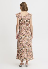 Blomstrede maxi-kjole i pink, sort og creme med korte flæseærmer og V-udskæring i ryggen. Har en tætsiddende talje og en elegant, svajende skørt.