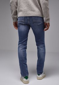 Úzké modré džíny s mírným vyblednutím, designem pěti kapes a jemnými švy. Nosené s lehkým šedým pleteným svetrem a bílými teniskami.