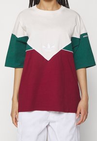 Färgblockerad t-shirt med beige, grön och burgundy sektioner, med rund halsringning och korta ärmar. Central logotyp sydd i vitt.