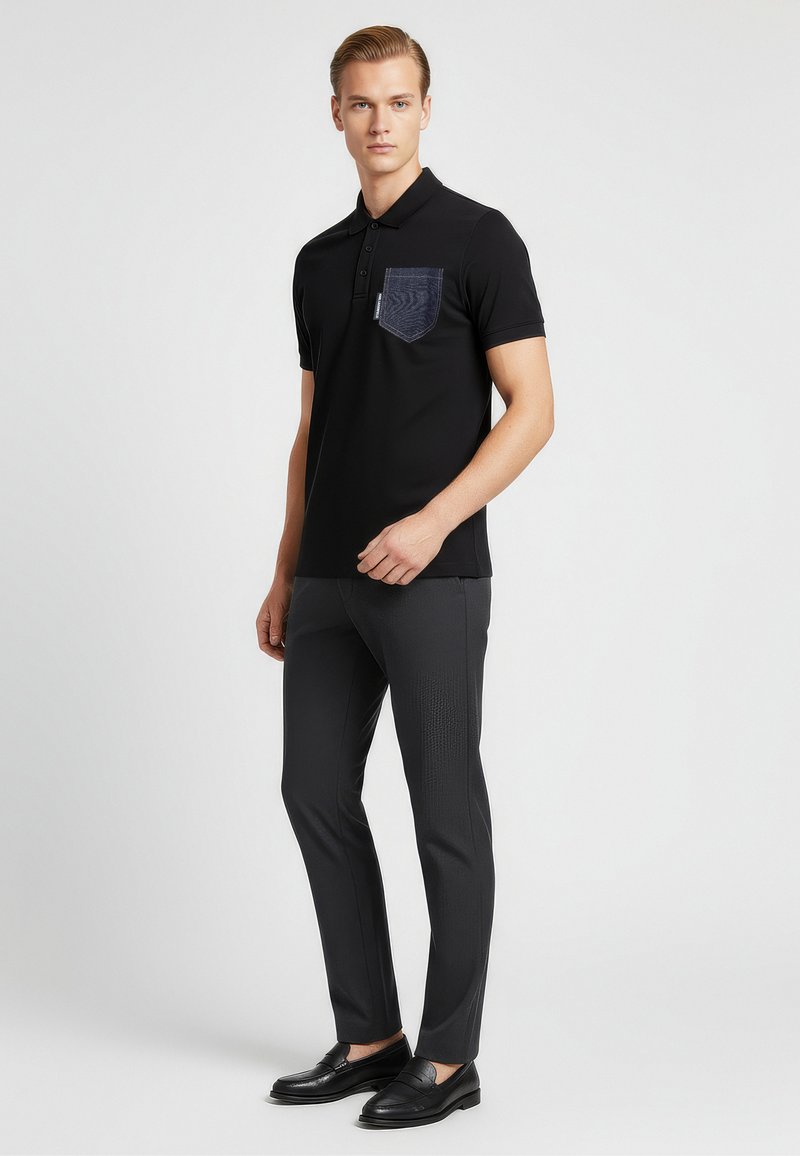 Černé polo triko s texturovanou džínovou kapsou, kombinované s tmavými úzkými kalhotami a černými mokasíny, na neutrálním pozadí.