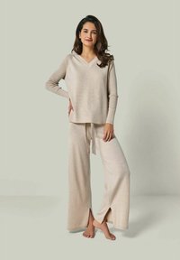 Beige knit lounge set featuring a v-neck long-sleeve top and wide-leg pants with side slits, made from soft, textured fabric.