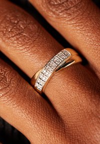 Een gouden ring met een rij heldere, sprankelende diamanten in een kanaalontwerp, geplaatst op textuur bruin huid.