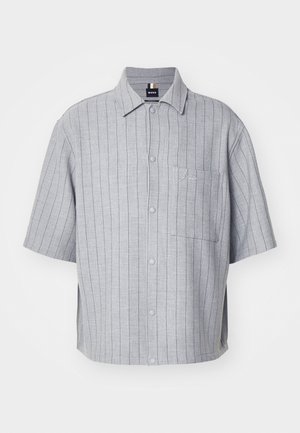 Īsām piedurknēm ar pogām krekls gaiši pelēkā krāsā, ar vertikālām svītrām, krūšu kabatu un izšūtu logotipu. Izgatavots no gluda, viegla auduma.