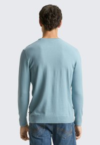 Lichtblauwe trui met lange mouwen en een ronde hals, geribbelde manchetten en een gladde textuur, gecombineerd met een blauwe spijkerbroek met gedetailleerde stiksels.