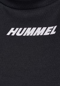 Logo HUMMEL blanc imprimé sur un tissu noir texturé, probablement des vêtements de sport ou de sport.