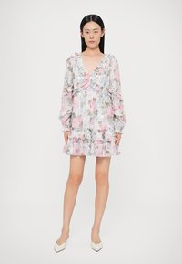 Rochie mini florală din material transparent cu flori pastelate roz și gri. Prezintă un decolteu și manșete cu volane, fustă în straturi și mâneci lungi.