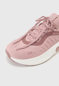 Világos rózsaszín sportcipő, strukturált szövet felsőrésszel, vastag fehér talppal, megerősített orral és hagyományos fűzőrendszerrel. Az Under Armour logó látható.