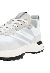 Biele a svetlošedé tenisky s vrchnou časťou z semišu a kože, s textúrovanými akcentmi, plochými šnúrkami a čiernou gumovou podrážkou. Viditeľné logo značky.