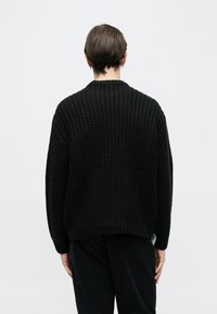 Pulover negru tricotat cu un design texturat, lejer și mâneci largi. Prezintă un decolteu rotund și tiv cu dungi.