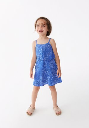 Vestido sin mangas azul con patrón de paisley, tela ligera, diseño en capas, largo hasta la rodilla, combinado con sandalias beige.