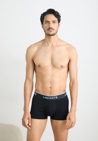 Black boxer briefs with a fitted design, featuring a branded waistband in white, made from a smooth, stretchy fabric.